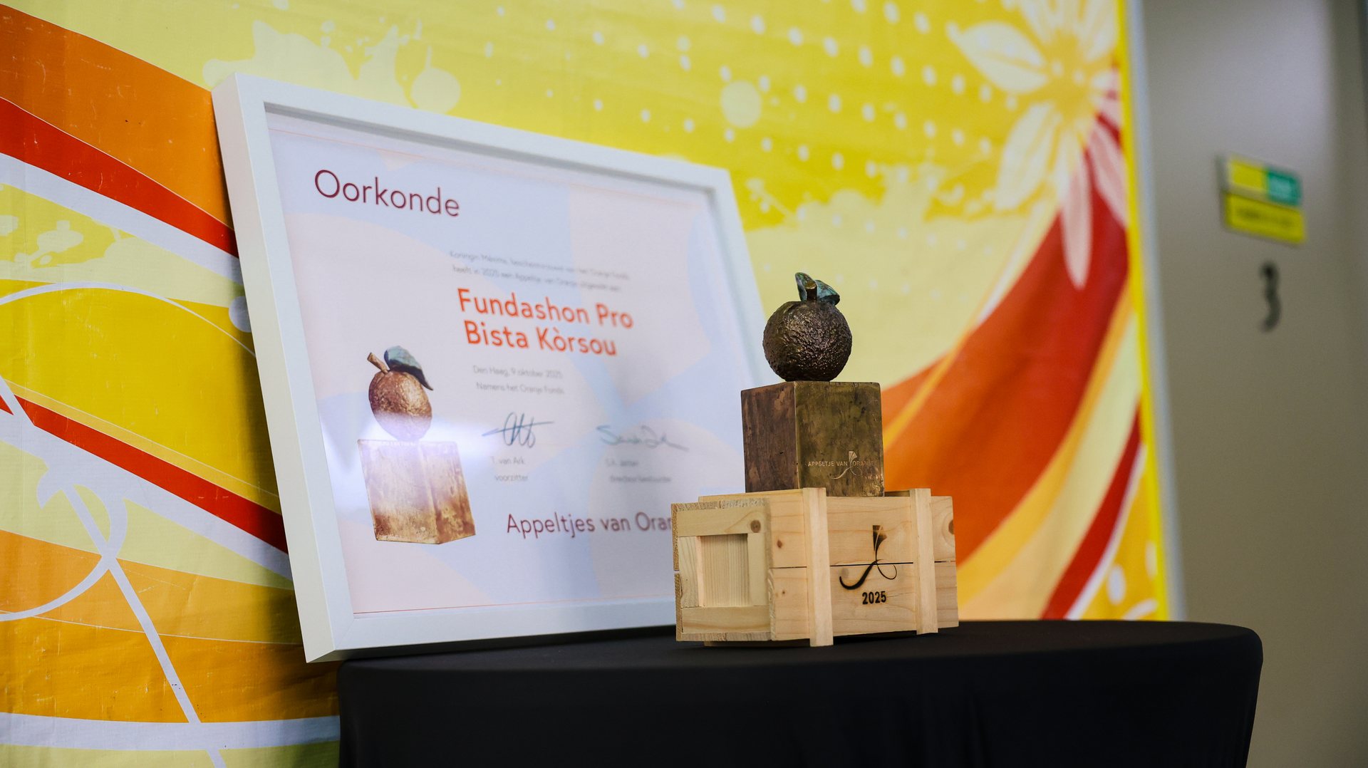 Banner van Fundashon Pro Bista Kòrsou naast het Appeltje van Oranje-beeldje